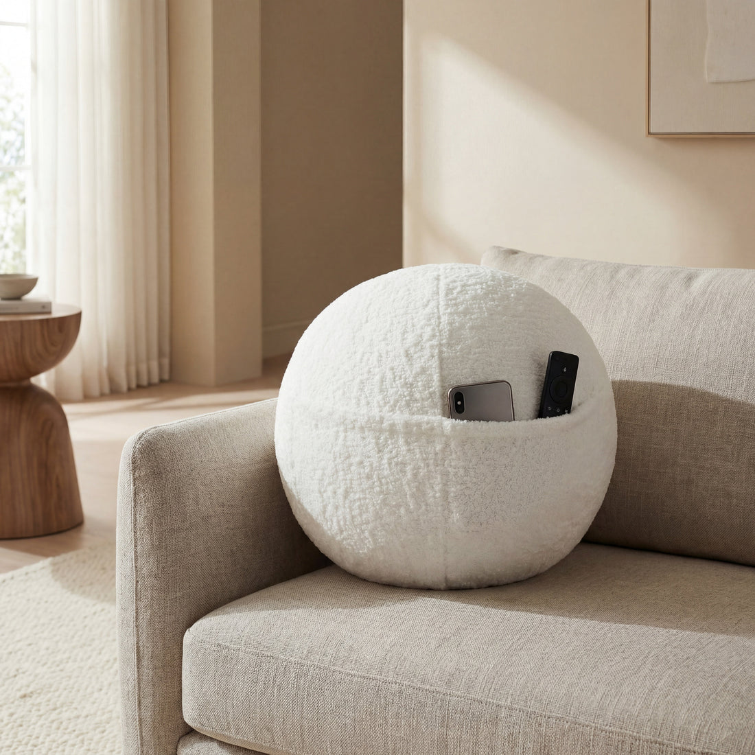 COZELA Orb bouclé sphere pillow on a couch with a phone and remote tucked into its hidden seam pocket
